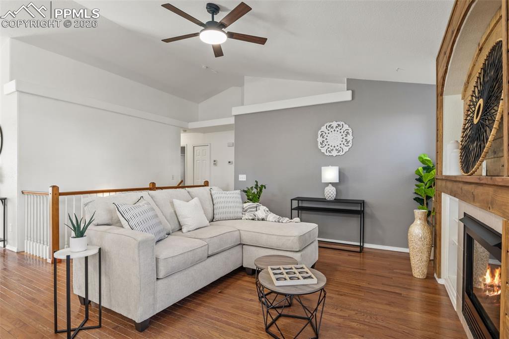 Living area featuring ceiling fan, a lit fireplace, vaulted ceiling, and wood finished floors