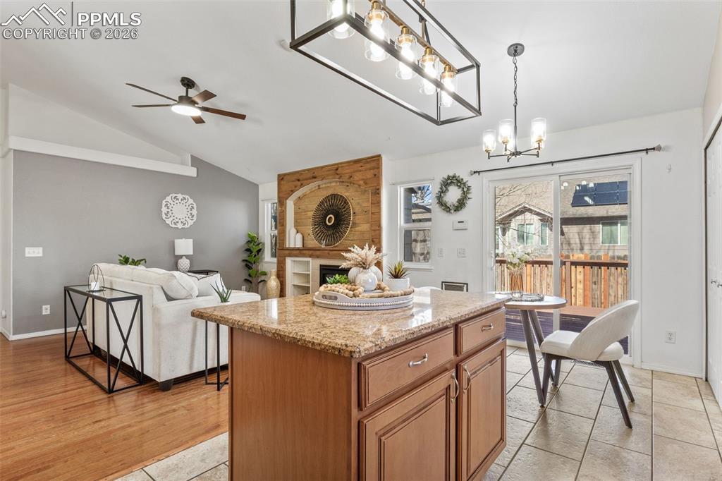 Kitchen with a kitchen island, light stone countertops, open floor plan, a ceiling fan, and wood finish cabinetry