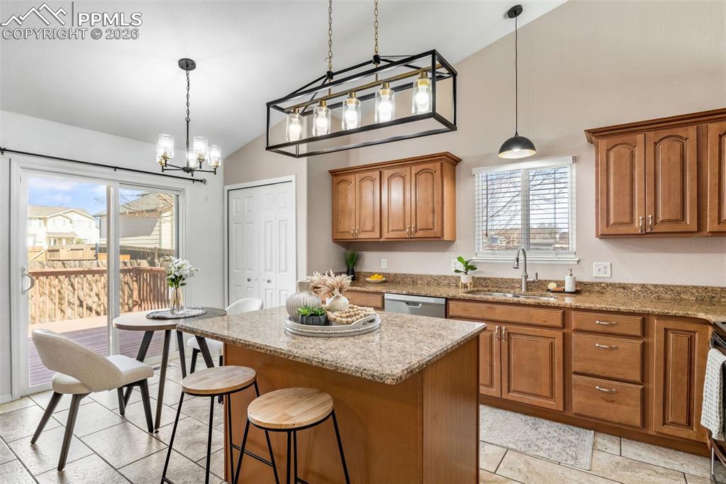 Kitchen with wood finish cabinetry, light stone countertops, a kitchen breakfast bar, a center island, and vaulted ceiling