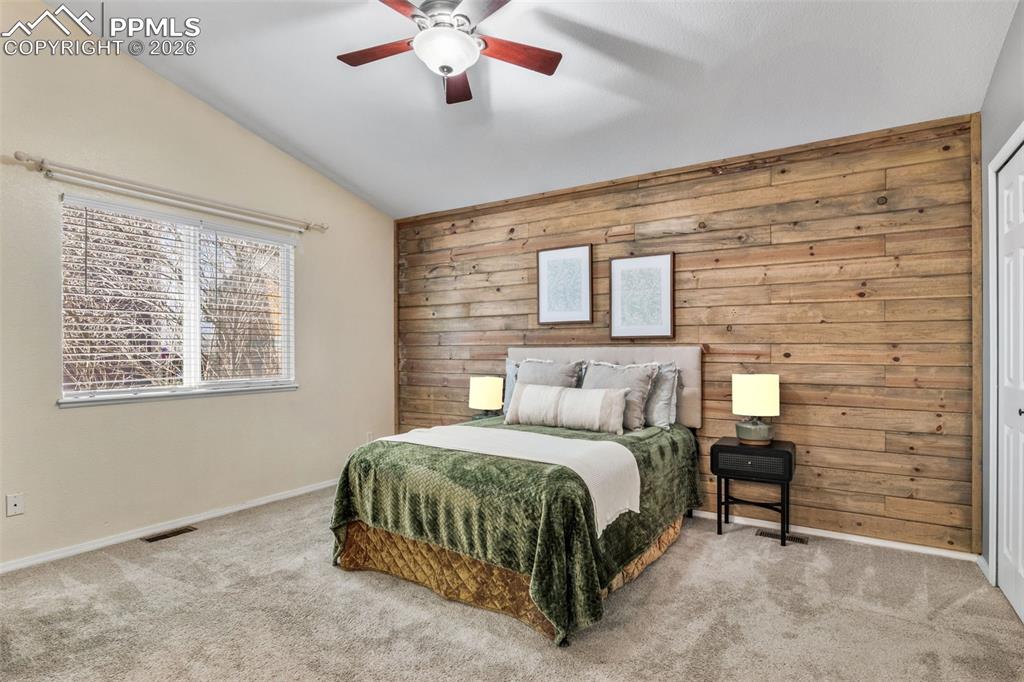 Carpeted bedroom with wood walls, vaulted ceiling, and a ceiling fan