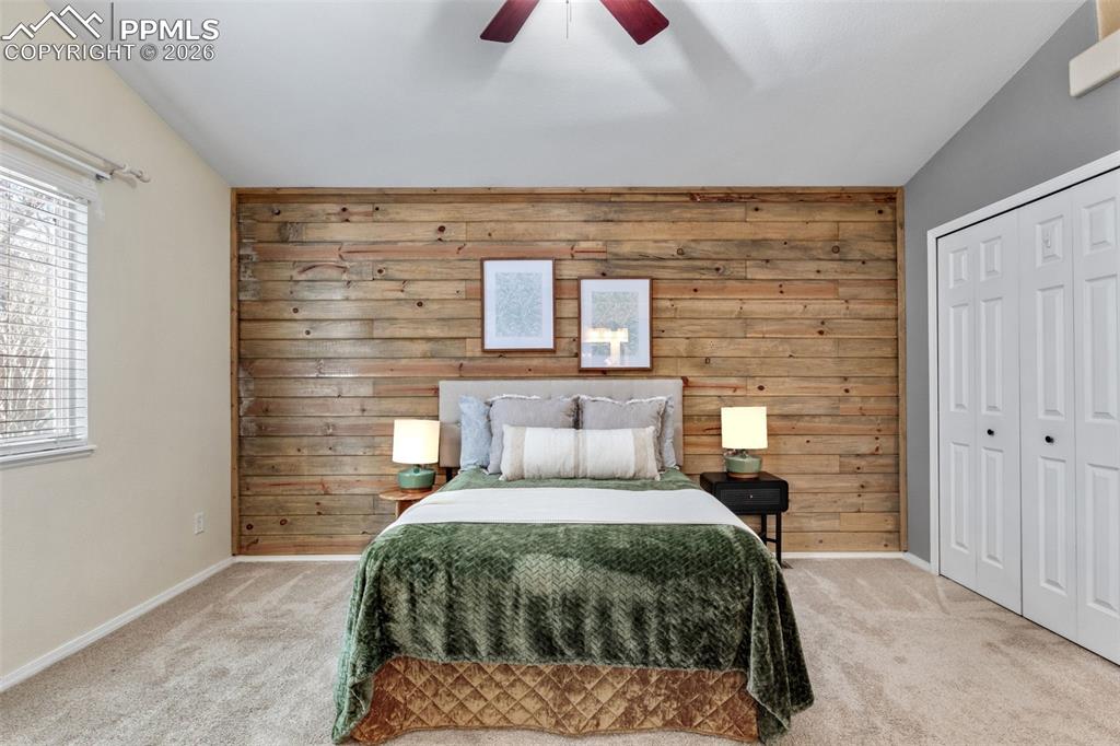 Carpeted bedroom with wooden walls, a closet, and a ceiling fan