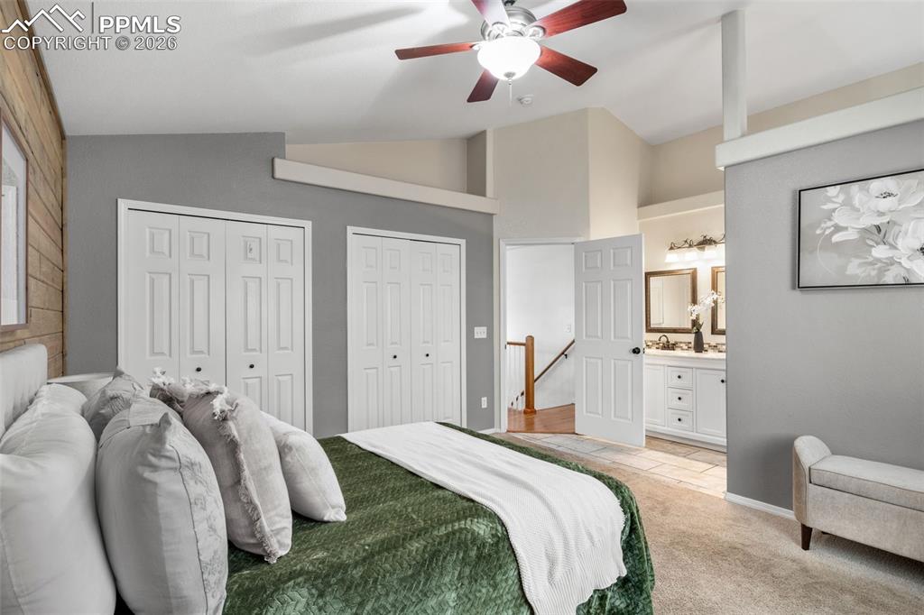 Bedroom featuring lofted ceiling, multiple closets, light colored carpet, a ceiling fan, and ensuite bath
