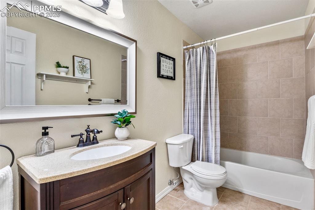 Full bath featuring vanity, a textured wall, shower / tub combo, and light tile patterned floors