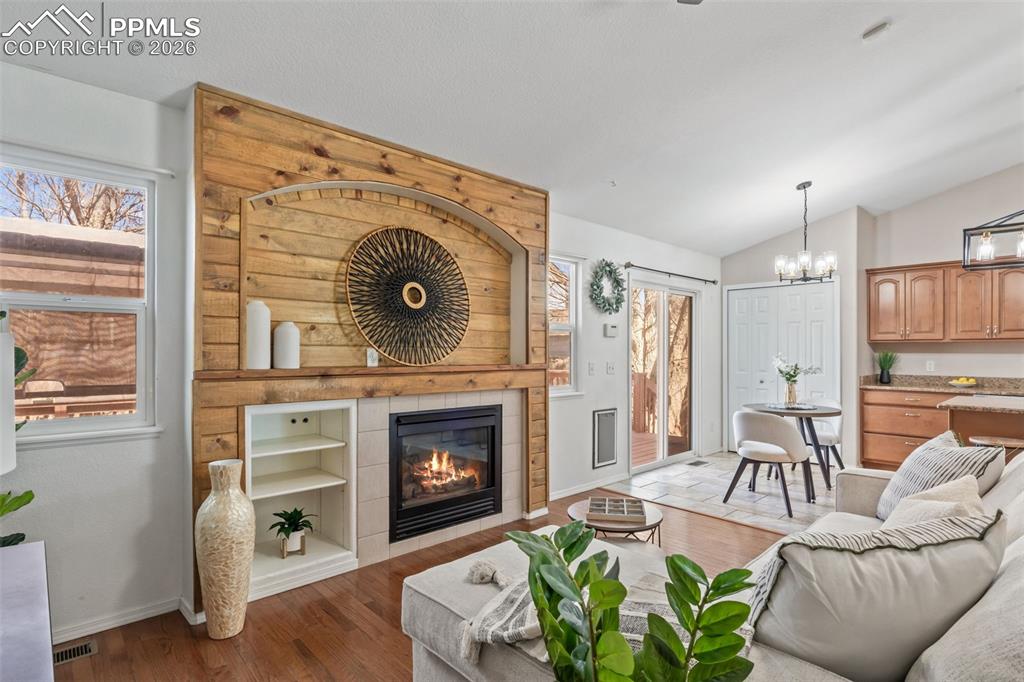 Living area with dark wood-style floors, a tiled fireplace, vaulted ceiling, and a chandelier