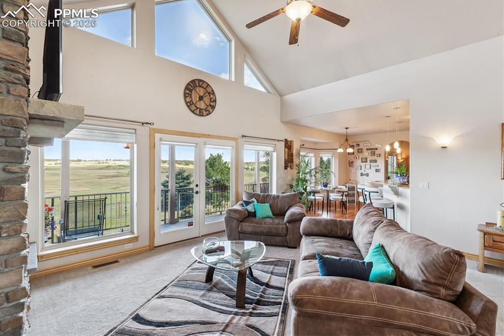 Living area with carpet flooring, high vaulted ceiling, french doors, a chandelier, and ceiling fan
