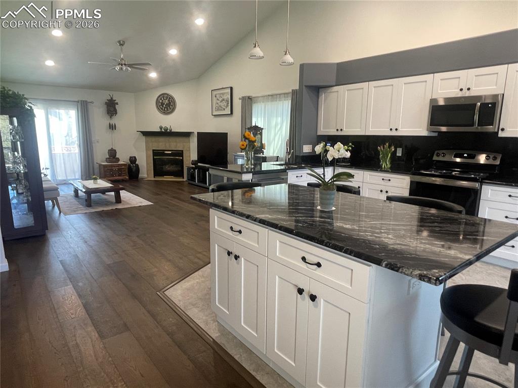 Kitchen with a breakfast bar, white cabinetry, dark stone counters, dark wood finished floors, and stainless steel appliances