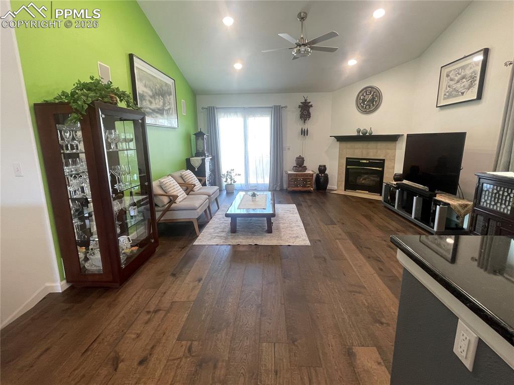 Living room with a fireplace, a ceiling fan, vaulted ceiling, dark wood-style flooring, and recessed lighting
