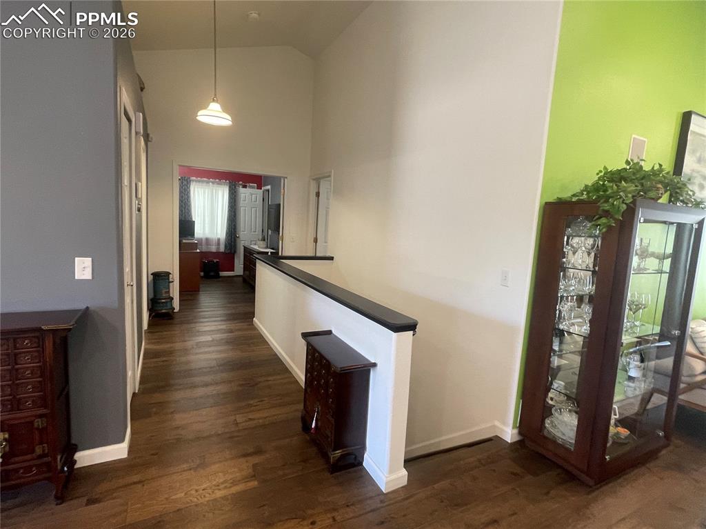 Corridor with dark wood-style flooring, vaulted ceiling, and an upstairs landing