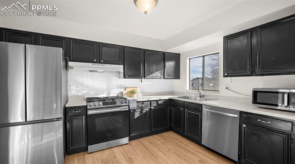 Kitchen featuring dark cabinetry, stainless steel appliances, light countertops, and light wood-style floors