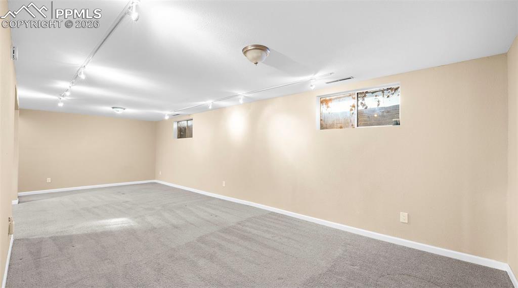 Below grade area featuring rail lighting and light colored carpet