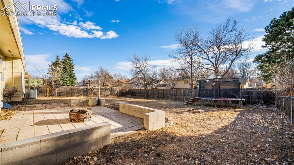 Fenced backyard featuring a patio, a trampoline, a fire pit, and a residential view