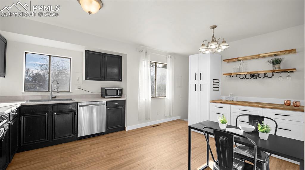 Kitchen with dark cabinets, stainless steel appliances, suspended lighting, and light wood-style flooring