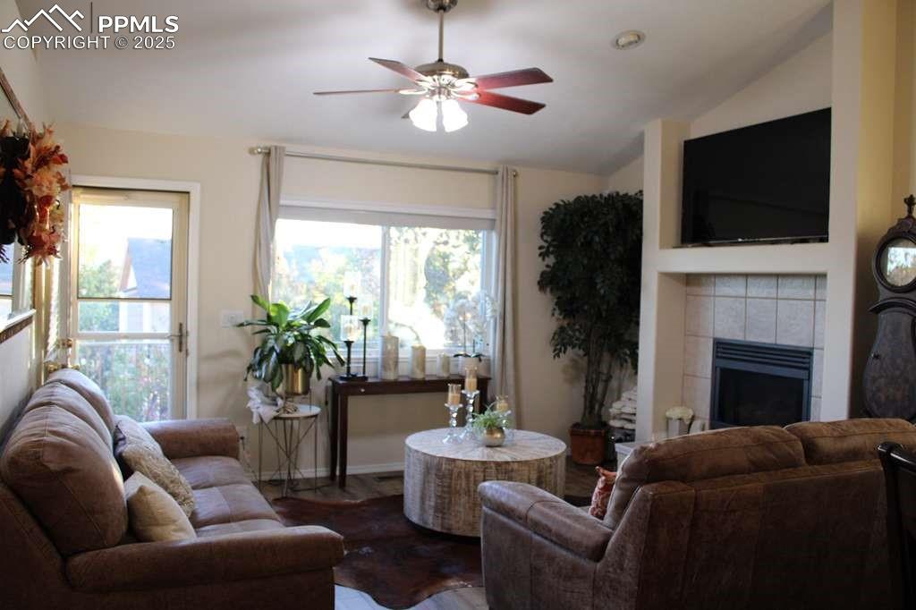 Living area with a tiled fireplace, ceiling fan, lofted ceiling, and wood finished floors