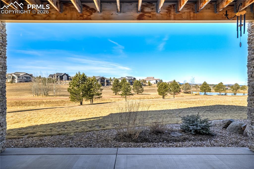 Shaded walk-out patio beneath the elevated deck, offering seamless indoor-outdoor flow with open land + pond backdrop.
