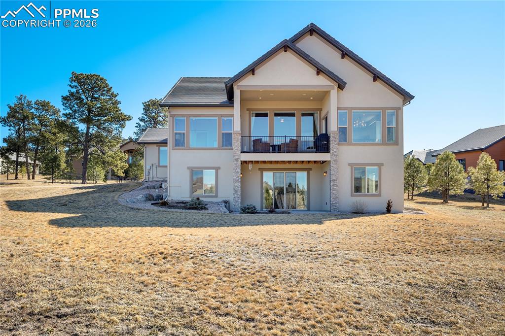 Elevated rear façade showcasing covered composite deck above walk-out patio—framed by open land, pond and mountain horizon.