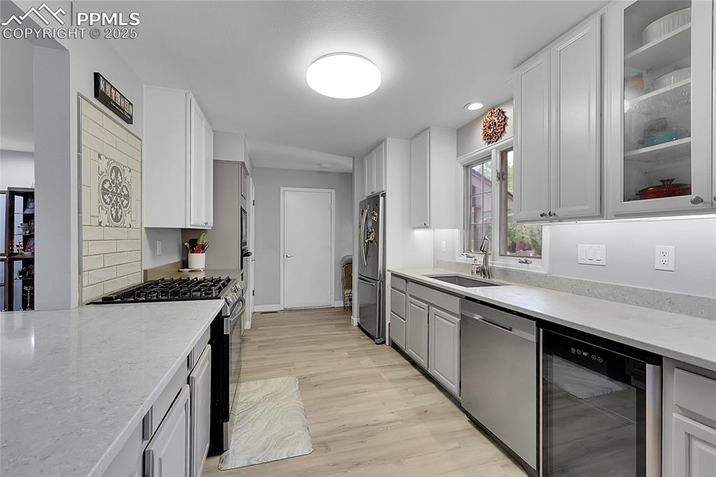 Kitchen featuring appliances with stainless steel finishes, wine cooler, light stone countertops, light wood-style floors, and white cabinetry