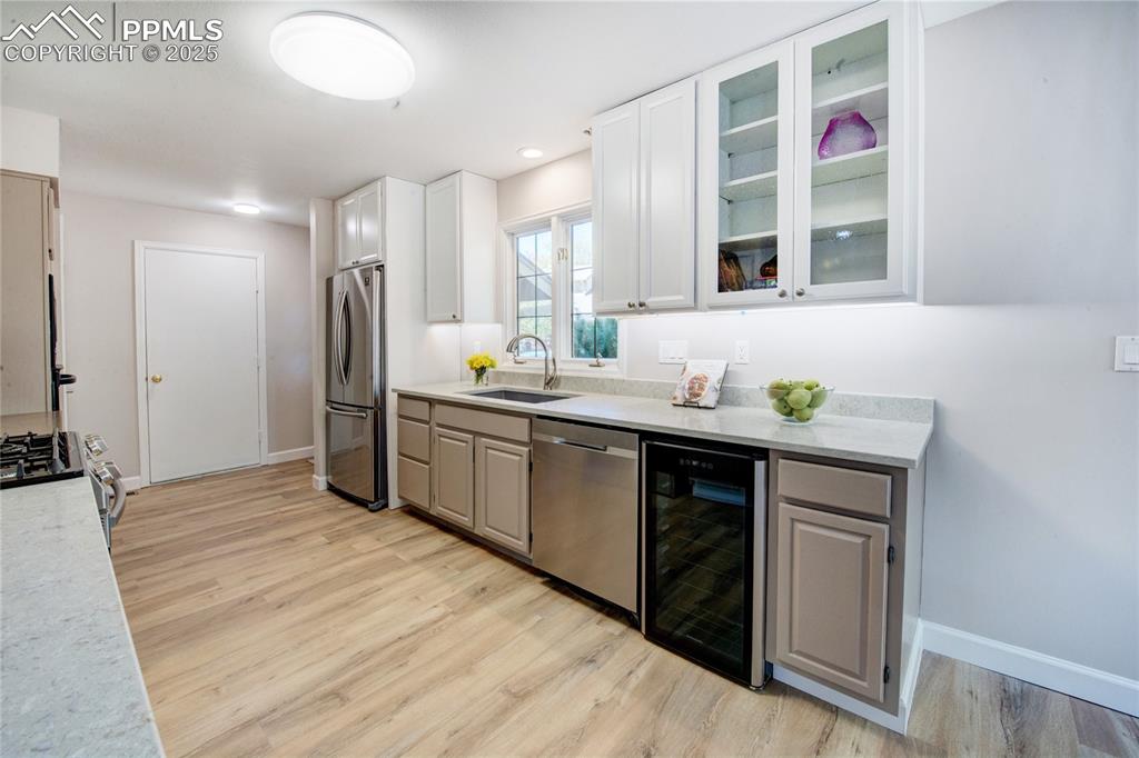 Kitchen featuring stainless steel appliances, beverage cooler, light wood-style floors, and light countertops
