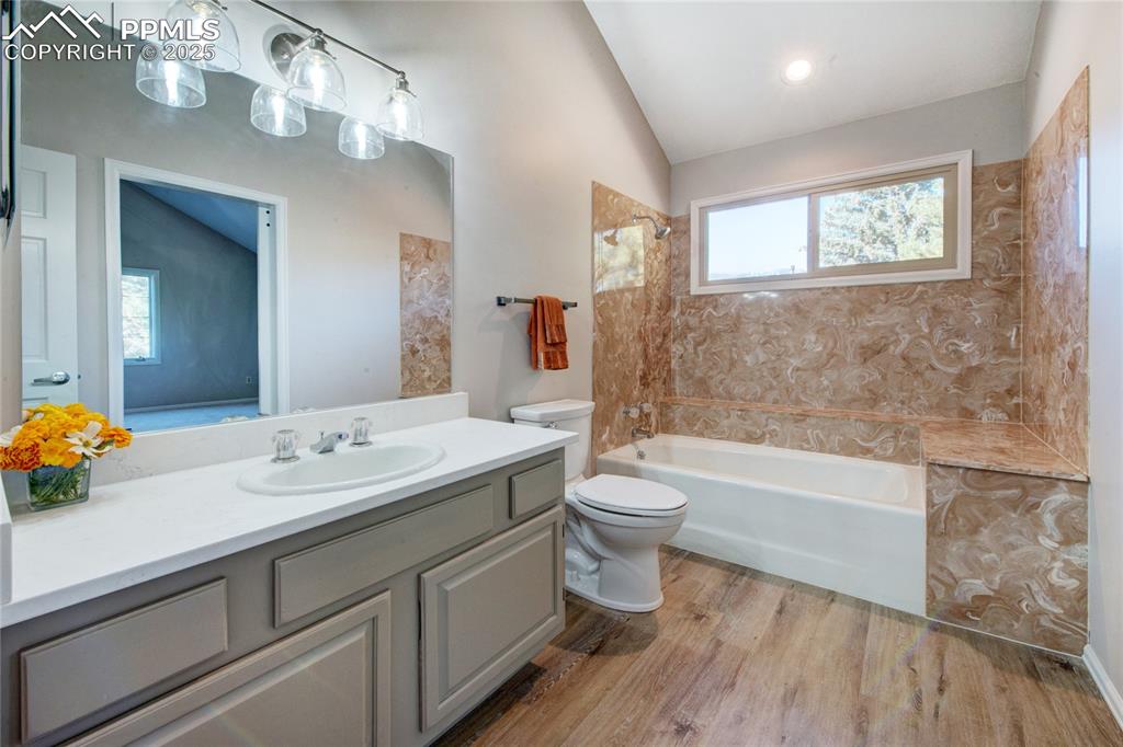 Full bathroom with vaulted ceiling, washtub / shower combination, vanity, plenty of natural light, and wood finished floors