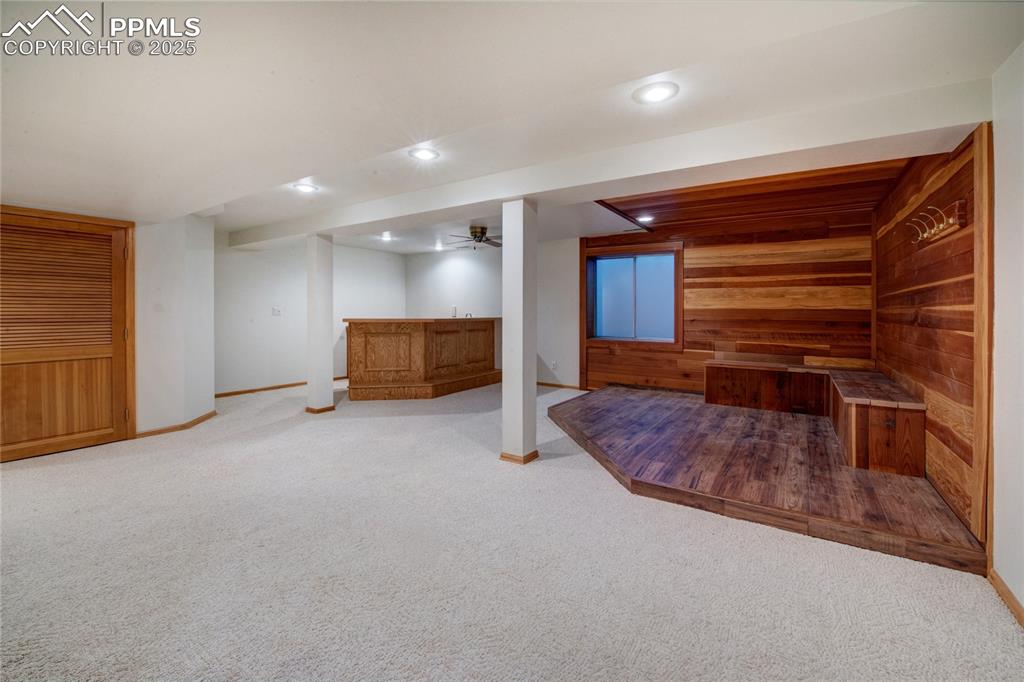 Finished below grade area featuring wooden walls, bar, light carpet, and recessed lighting