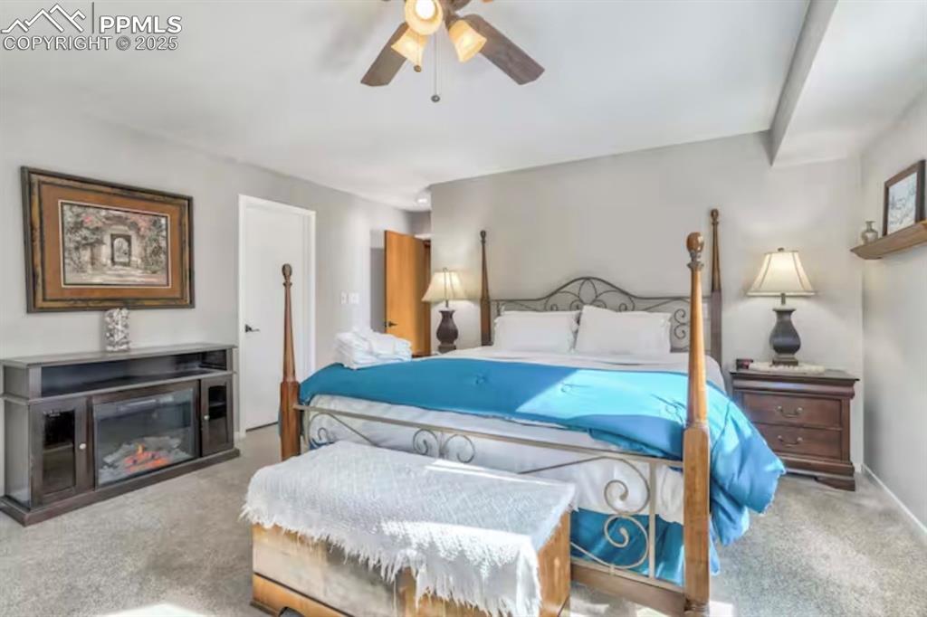 Carpeted bedroom featuring a ceiling fan and a glass covered fireplace