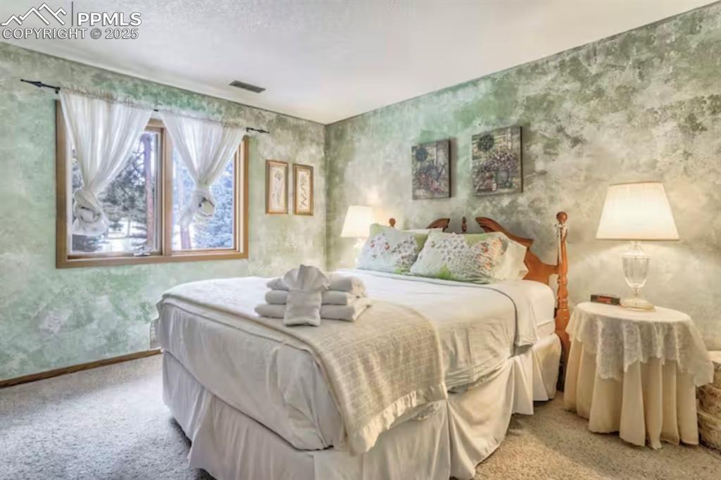 Bedroom with wallpapered walls, carpet flooring, and a textured ceiling