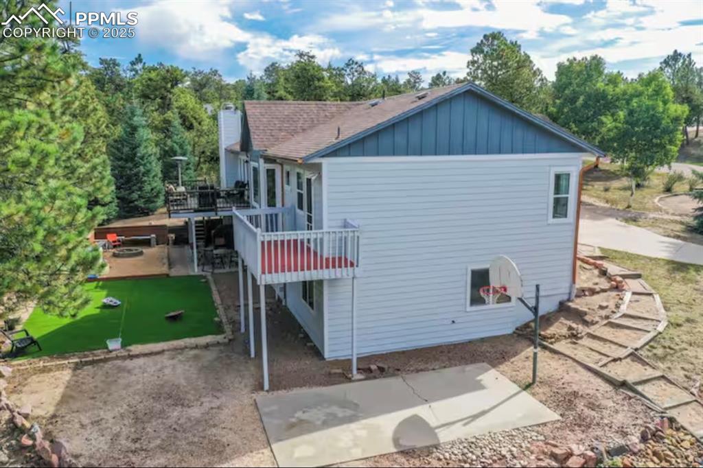 View of side of home with a wooden deck, a patio area, board and batten siding, and roof with shingles