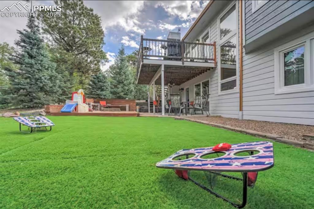 View of grassy yard featuring a wooden deck and a patio area
