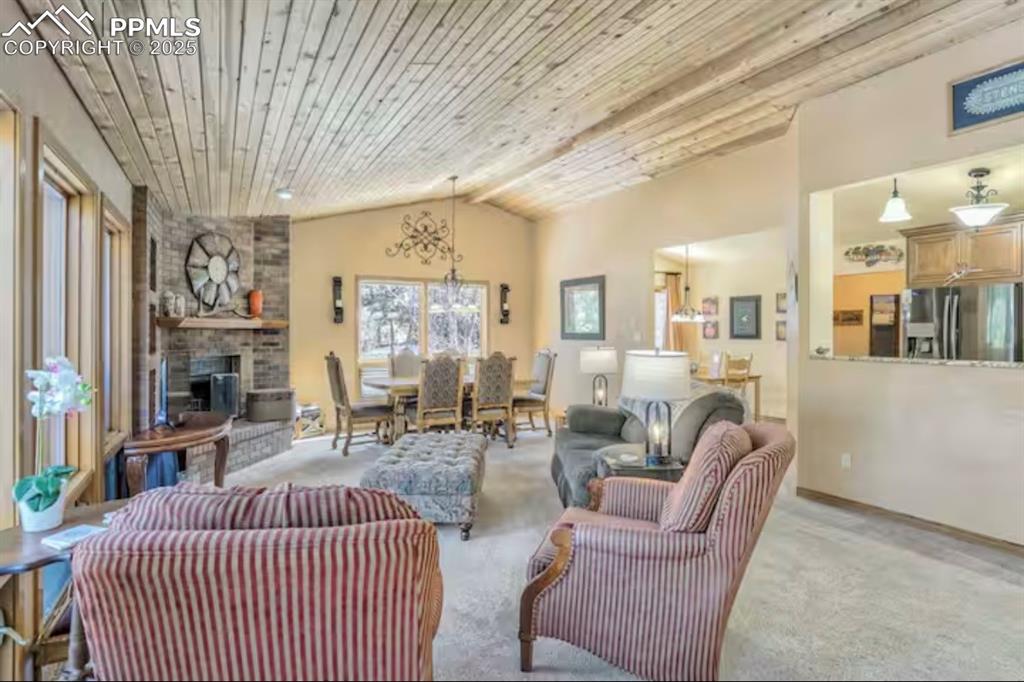 Living area featuring vaulted ceiling, wooden ceiling, carpet floors, and a fireplace