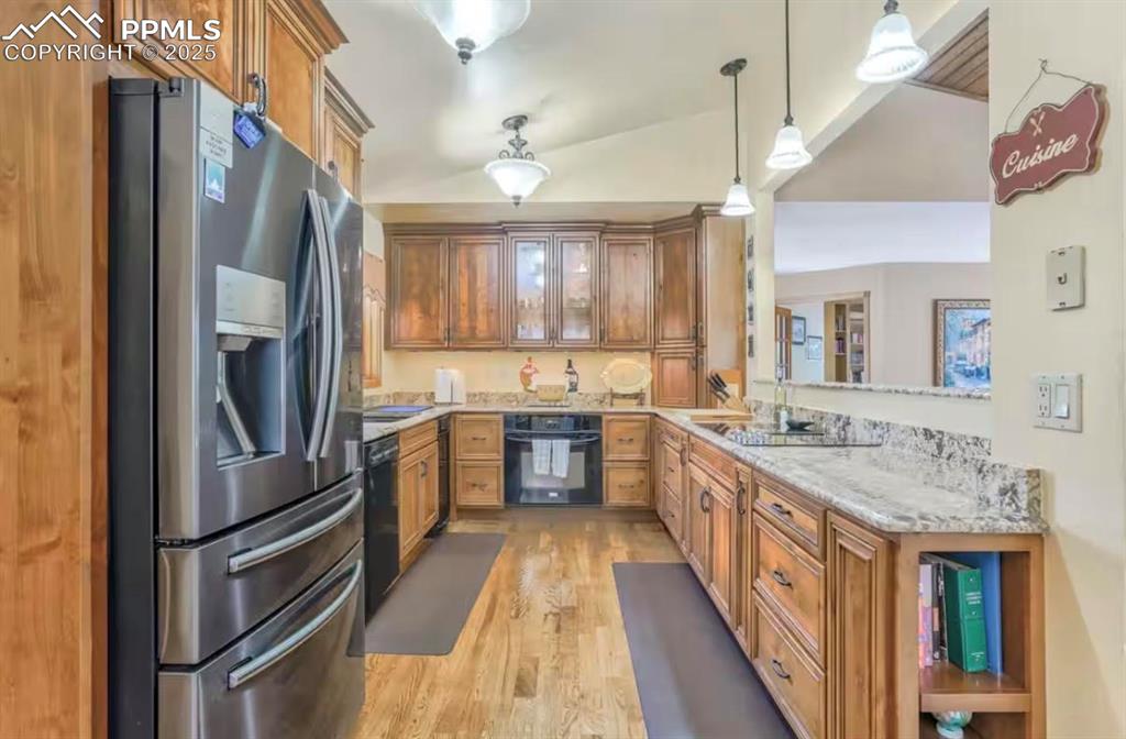Kitchen with black appliances, brown cabinetry, pendant lighting, light wood-type flooring, and lofted ceiling