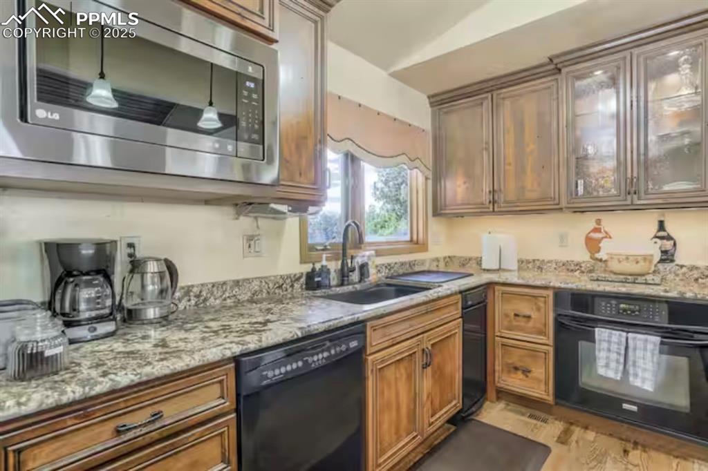 Kitchen with black appliances, light stone countertops, brown cabinets, and light wood finished floors