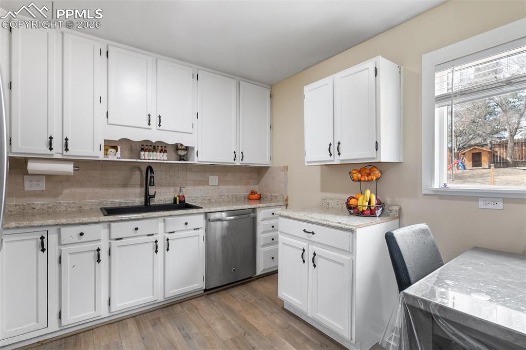 Kitchen with white cabinets, dishwasher, open shelves, light wood finished floors, and backsplash