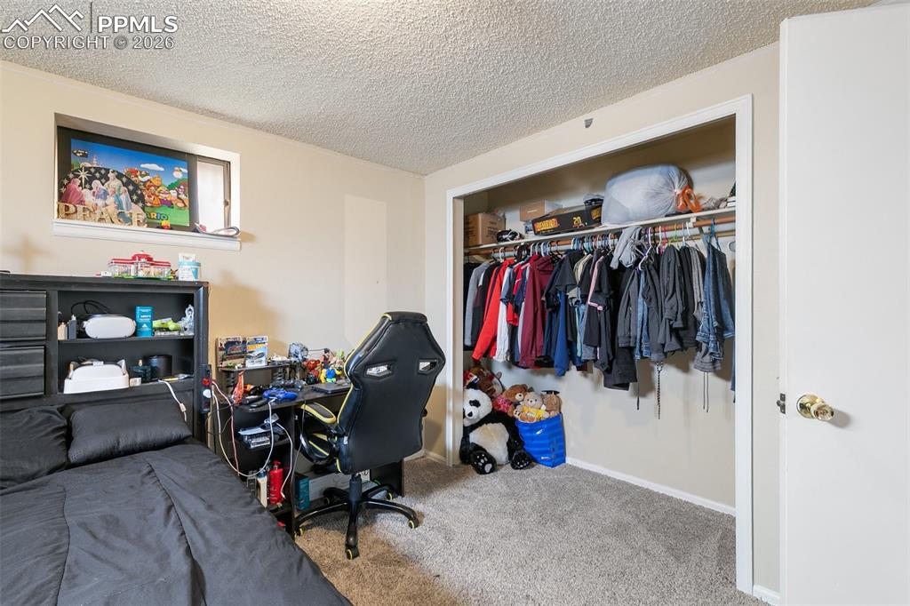 Bedroom with a textured ceiling, carpet flooring, a closet, and a desk