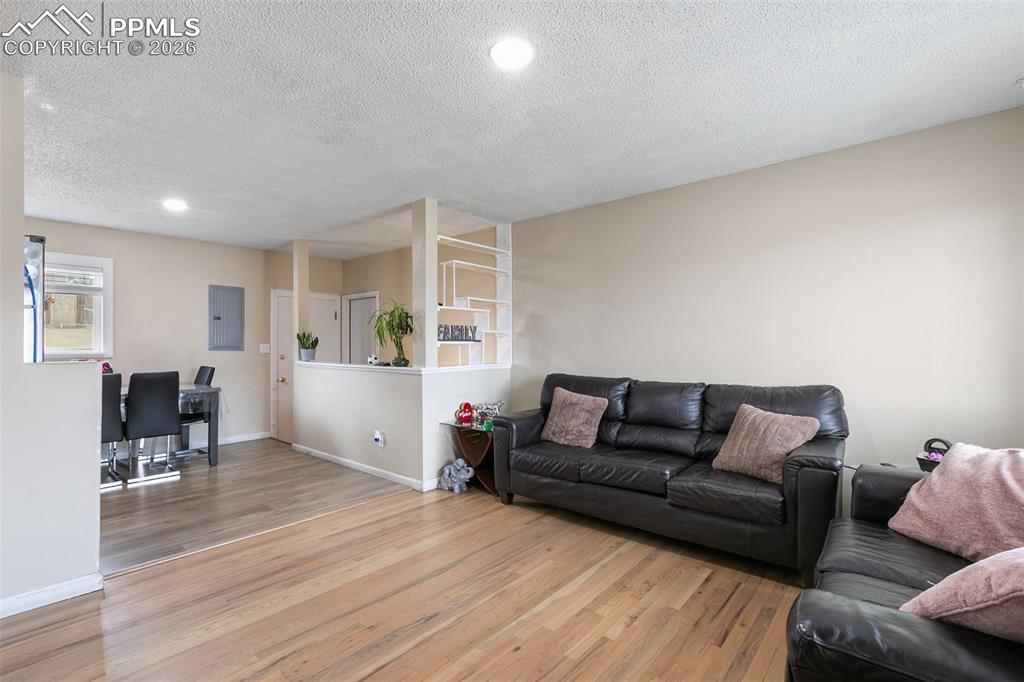 Living area with wood finished floors, a textured ceiling, recessed lighting, and electric panel