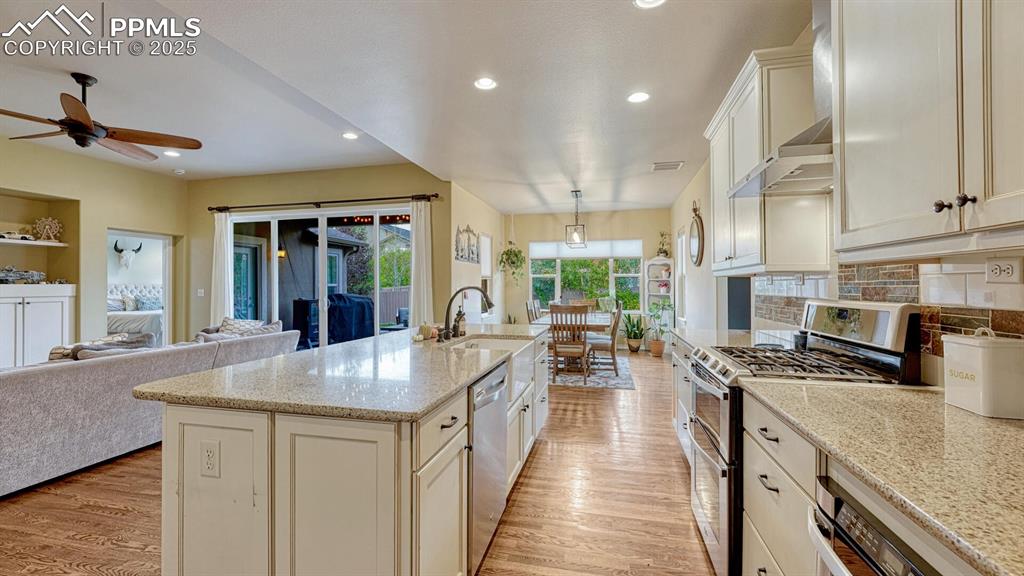 Kitchen featuring stainless steel appliances, open floor plan, recessed lighting, light stone countertops, and wall chimney range hood
