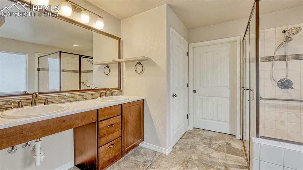 Bathroom with a shower stall, double vanity, and backsplash
