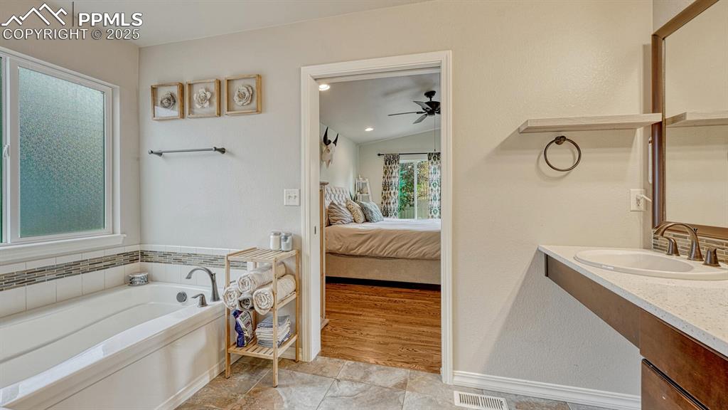 Bathroom featuring a garden tub, vanity, lofted ceiling, ensuite bath, and a ceiling fan