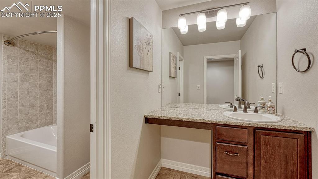 Bathroom featuring a textured wall, washtub / shower combination, and vanity