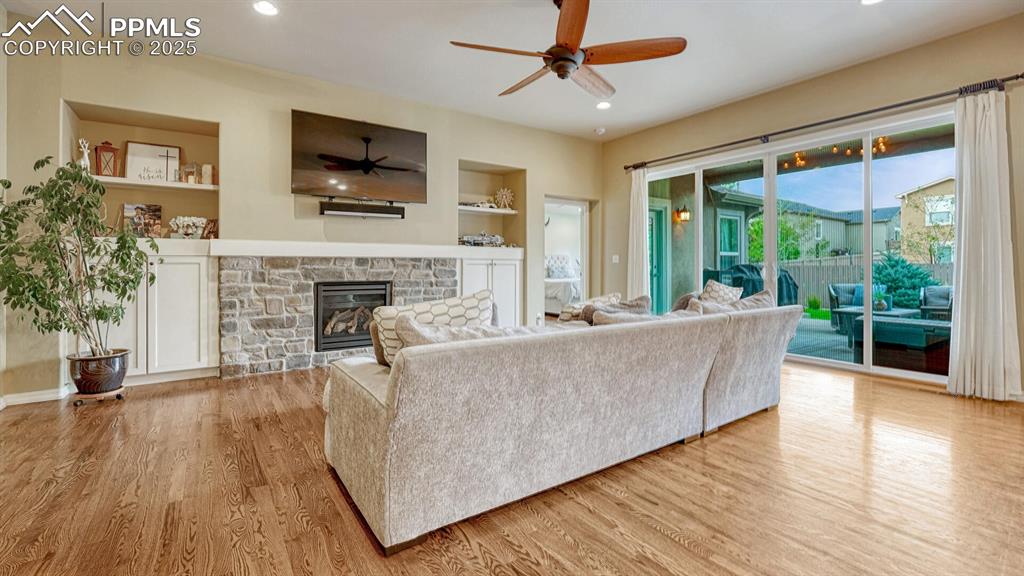 Living area with built in features, recessed lighting, a stone fireplace, light wood finished floors, and ceiling fan