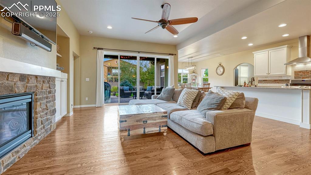 Living area with light wood-style floors, recessed lighting, a stone fireplace, ceiling fan, and arched walkways