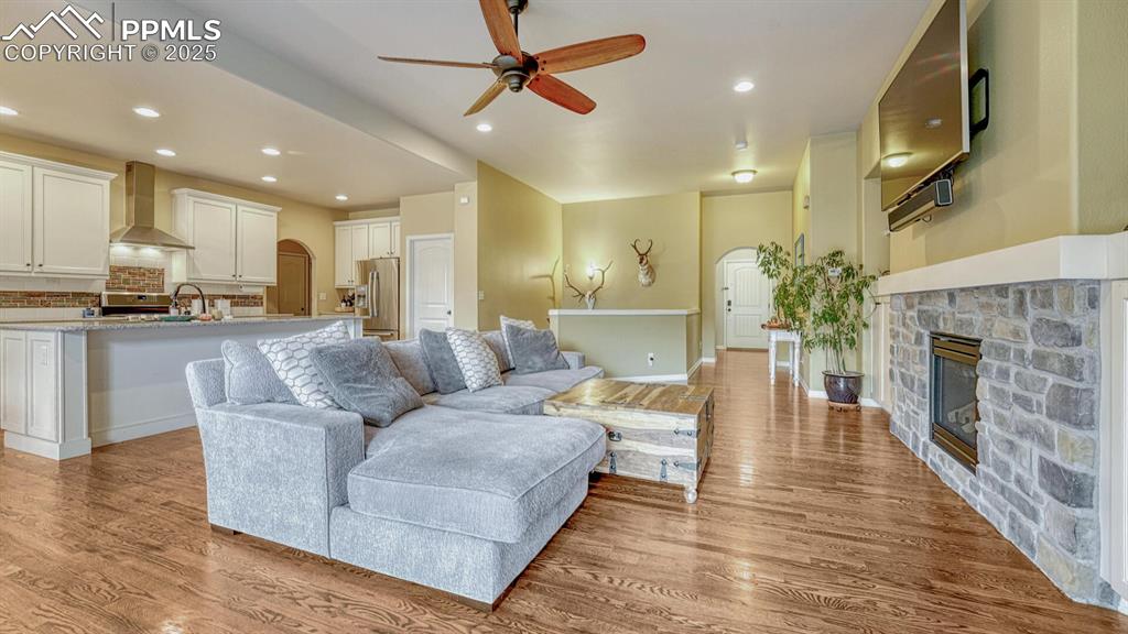 Living room featuring recessed lighting, arched walkways, a stone fireplace, light wood-style flooring, and ceiling fan