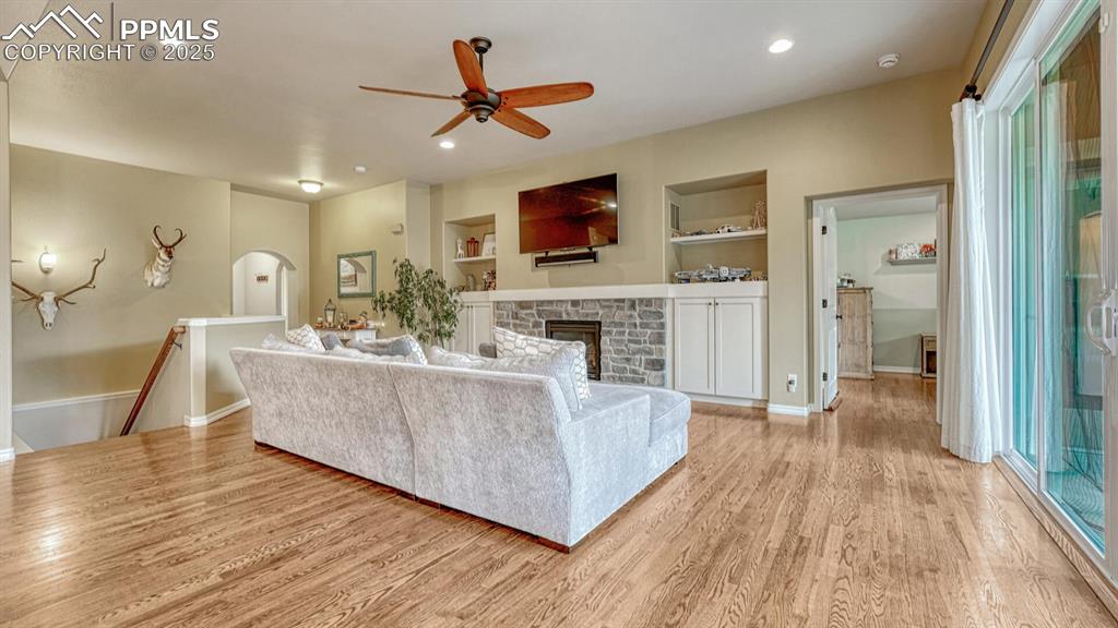 Living area with built in shelves, light wood-style flooring, recessed lighting, a ceiling fan, and arched walkways