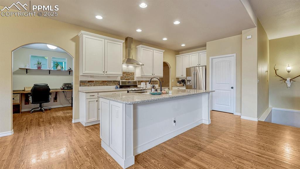 Kitchen with white cabinets, decorative backsplash, stainless steel appliances, an office area, and arched walkways