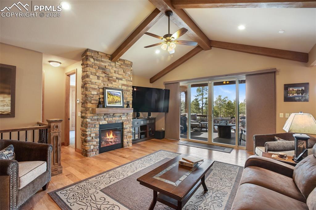 Living area with lofted ceiling with beams, light wood-style flooring, ceiling fan, and a fireplace
