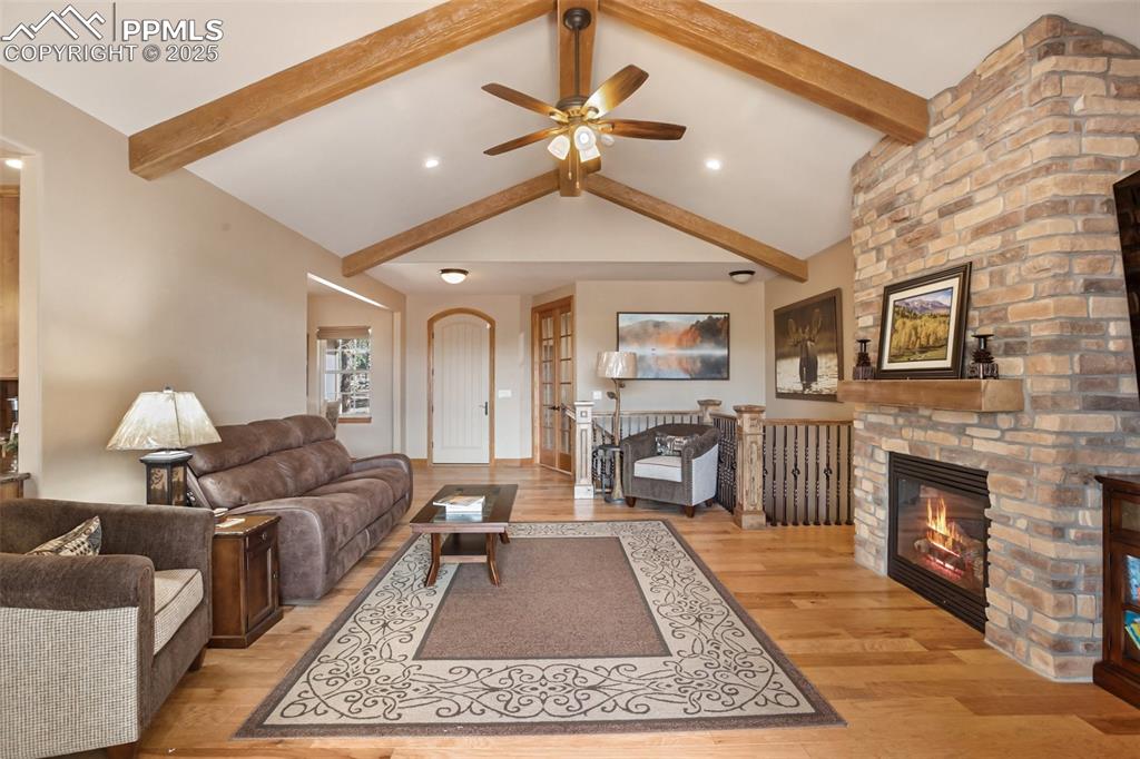 Living room featuring beam ceiling, ceiling fan, a fireplace, and light wood finished floors