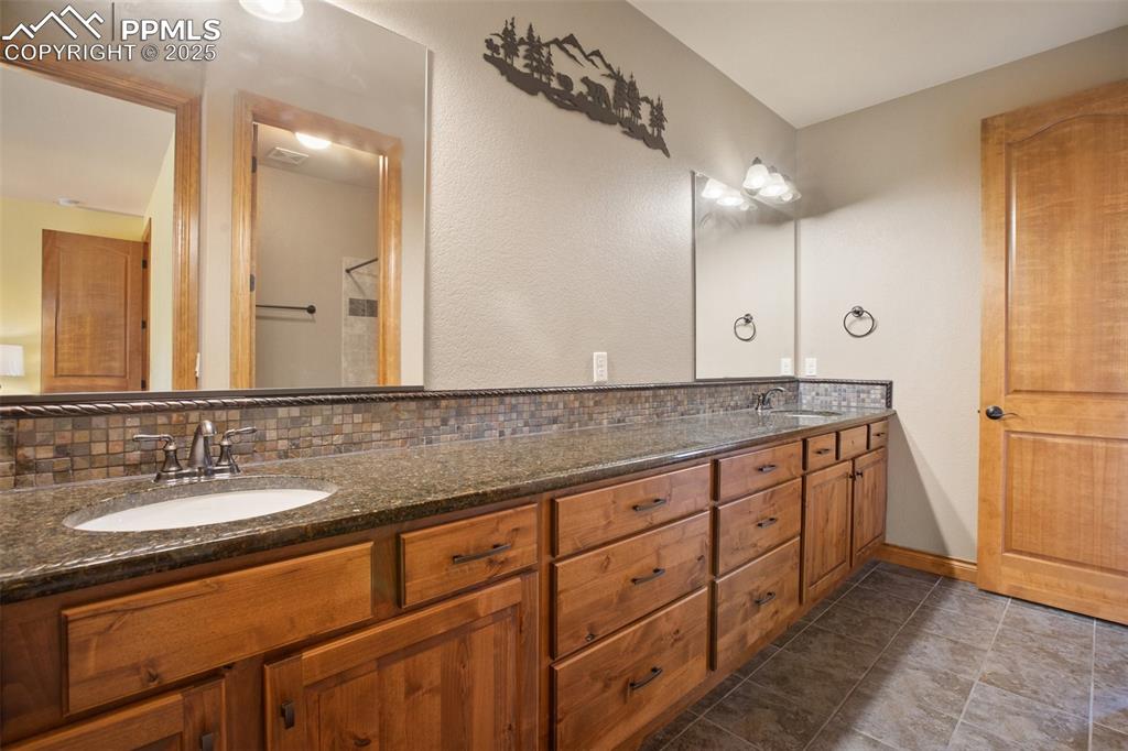 Bathroom with double vanity, baseboards, backsplash, and a sink