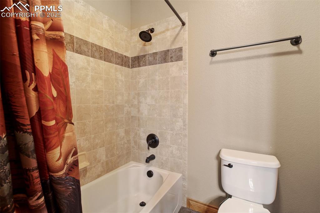 Bathroom with a textured wall, toilet, and shower / bath combination with curtain
