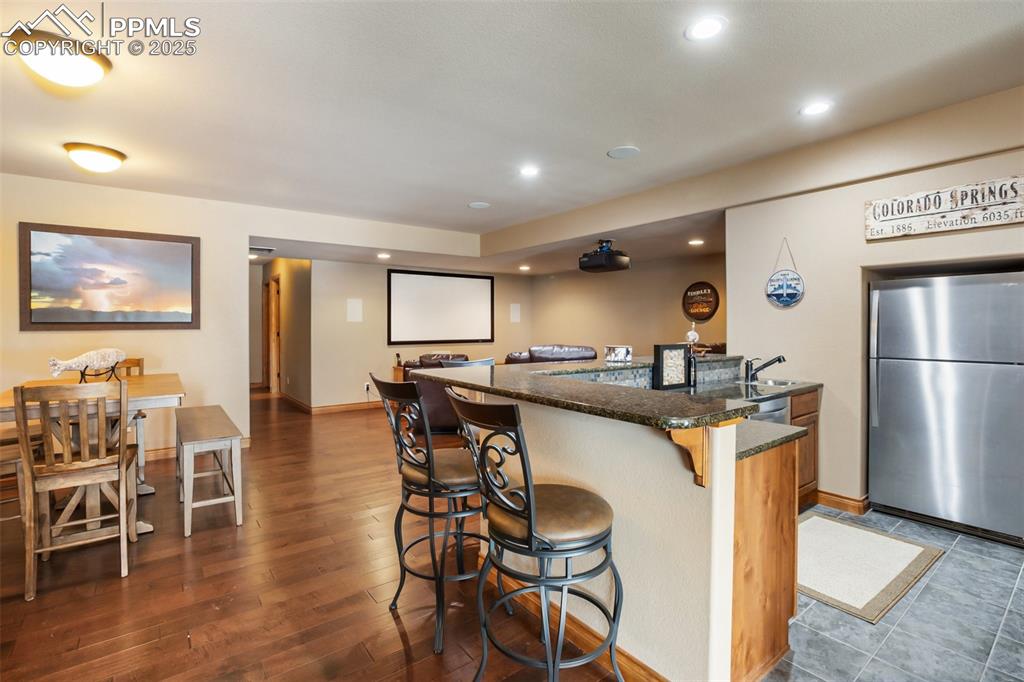 Kitchen featuring recessed lighting, dark stone countertops, a kitchen breakfast bar, freestanding refrigerator, and dark wood-style floors