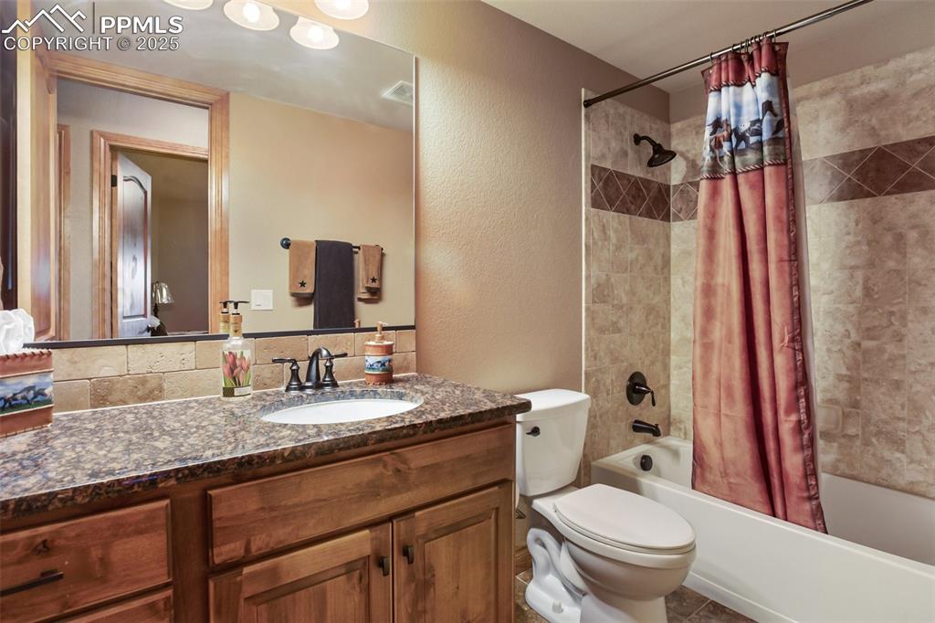 Full bathroom featuring vanity, visible vents, shower / bath combo, toilet, and a textured wall