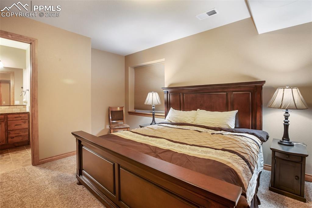 Bedroom with visible vents, baseboards, light colored carpet, and ensuite bathroom