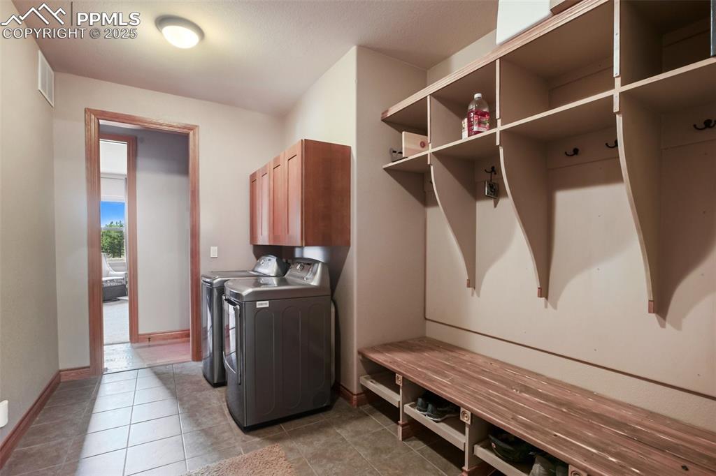 Clothes washing area featuring visible vents, washer and dryer, cabinet space, light tile patterned floors, and baseboards